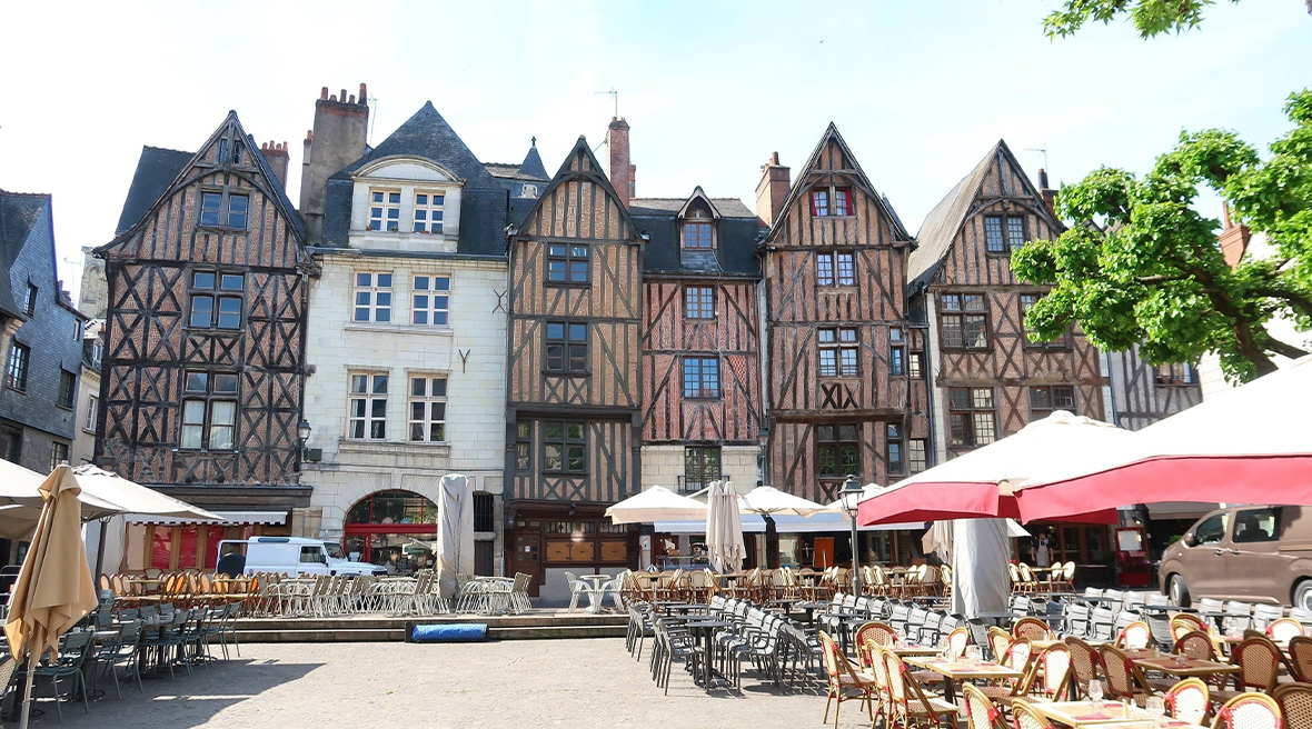 Tall and narrow half-timbered medieval buildings overlooking a public square laid out with restaurant tables